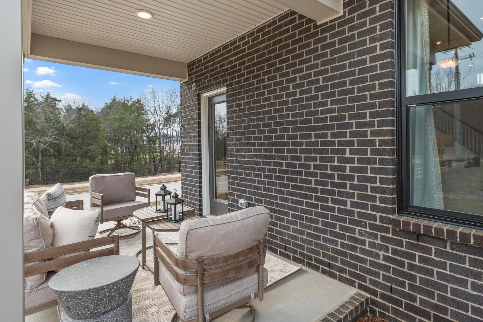 Covered outdoor patio at Benders Cove in Mt. Juliet, TN by Davidson Homes featuring lounge seating and brick exterior.