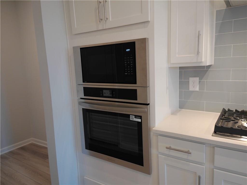 Modern kitchen featuring stainless steel double oven, gas cooktop, white shaker cabinets, and blue subway tile backsplash in Davidson Homes The Marion C, Winder, Georgia