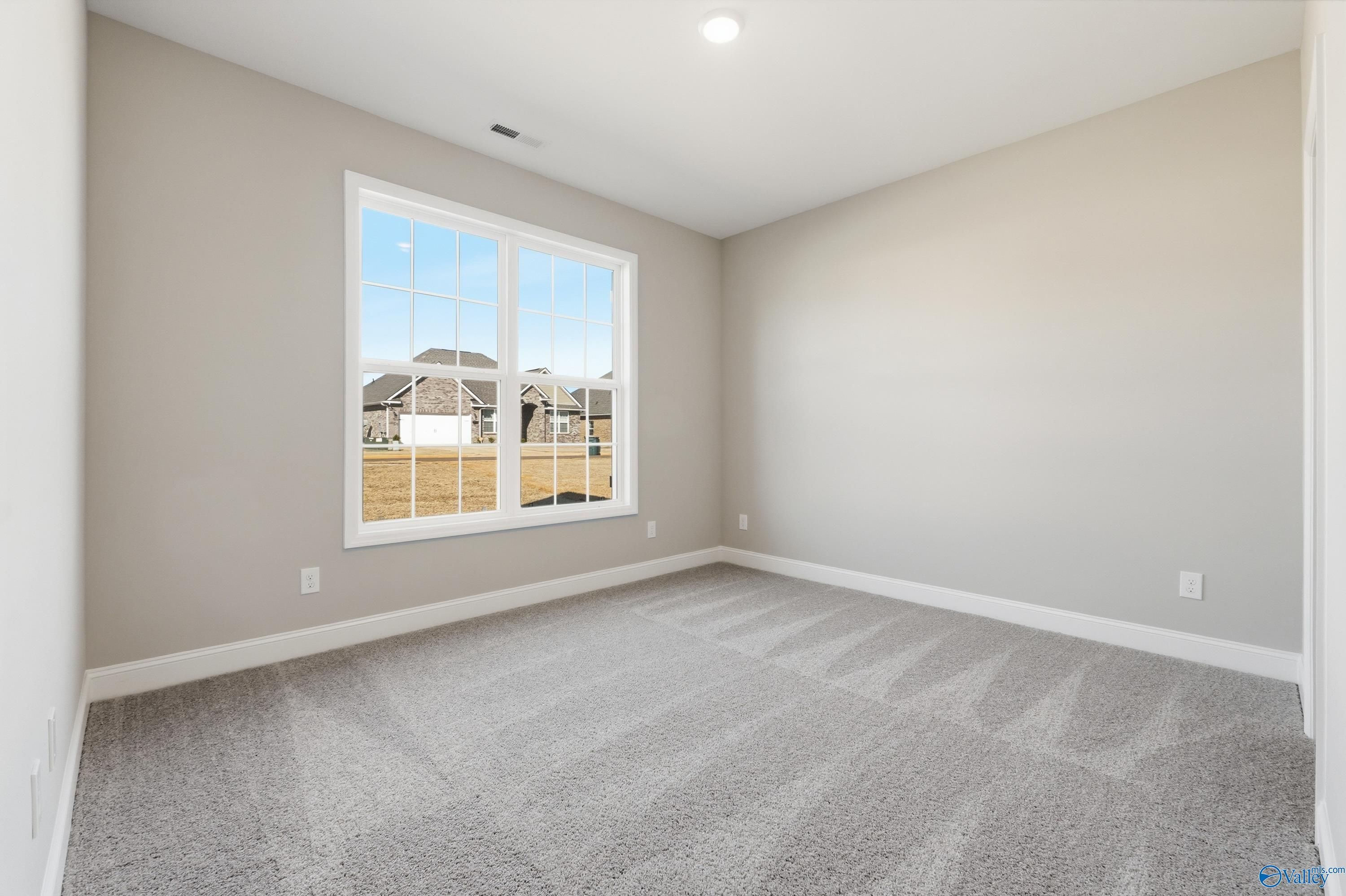 Bright bedroom with beige walls, gray carpet, and large window view of neighborhood in Davidson Homes The Rockford, Harvest, AL