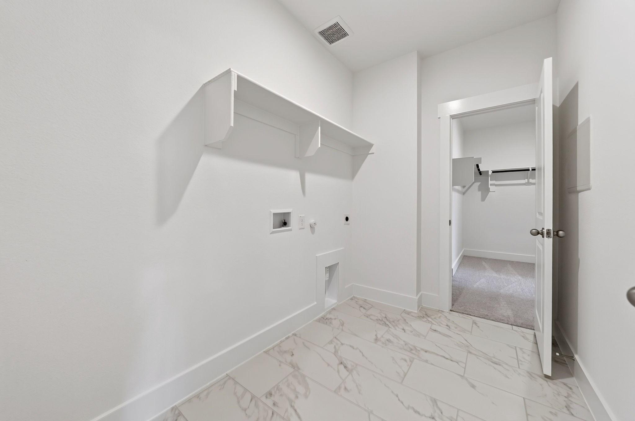 Bright utility room with marble-look tile flooring, wall shelving, and walk-in closet access in Davidson Homes The Holly F, Josephine, TX