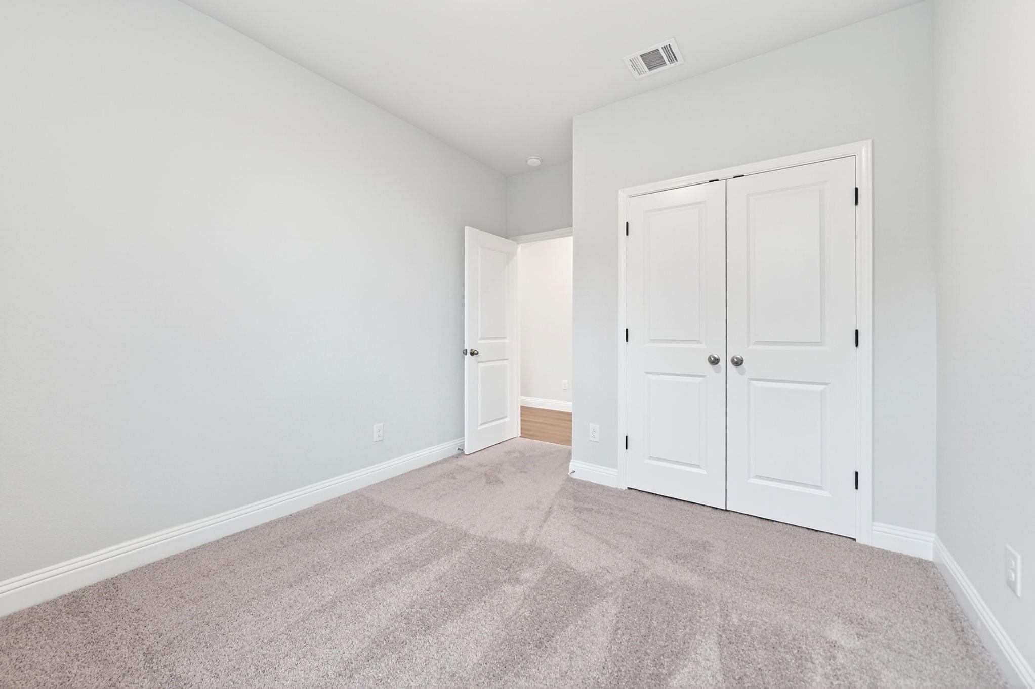 Spacious secondary bedroom in The Redbud plan featuring neutral wall colors, plush carpeting, and double-door closets.