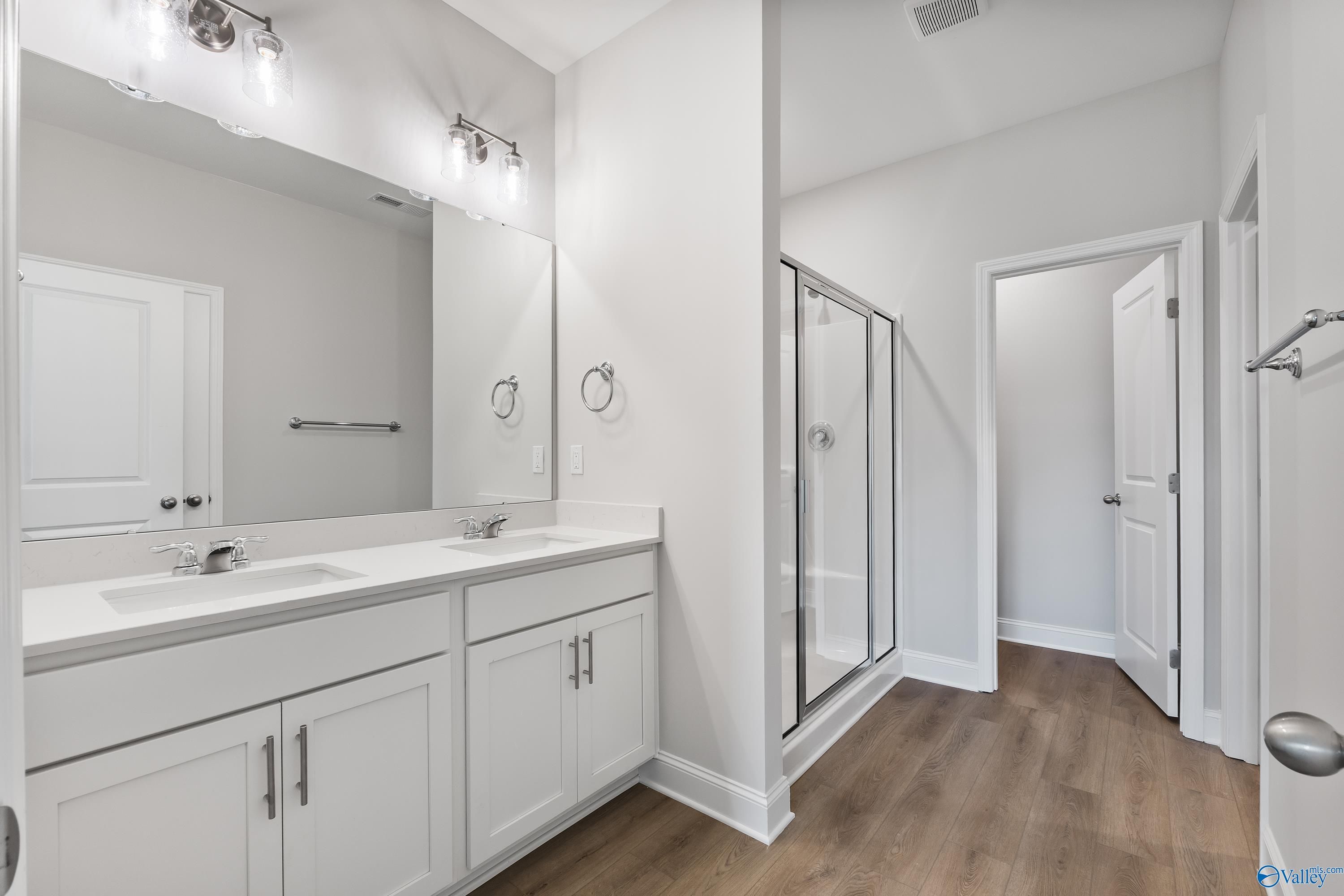 Modern master bathroom with double vanity, frameless glass shower, and luxury vinyl plank flooring in Davidson Homes The Daphne, Hazel Green, Alabama