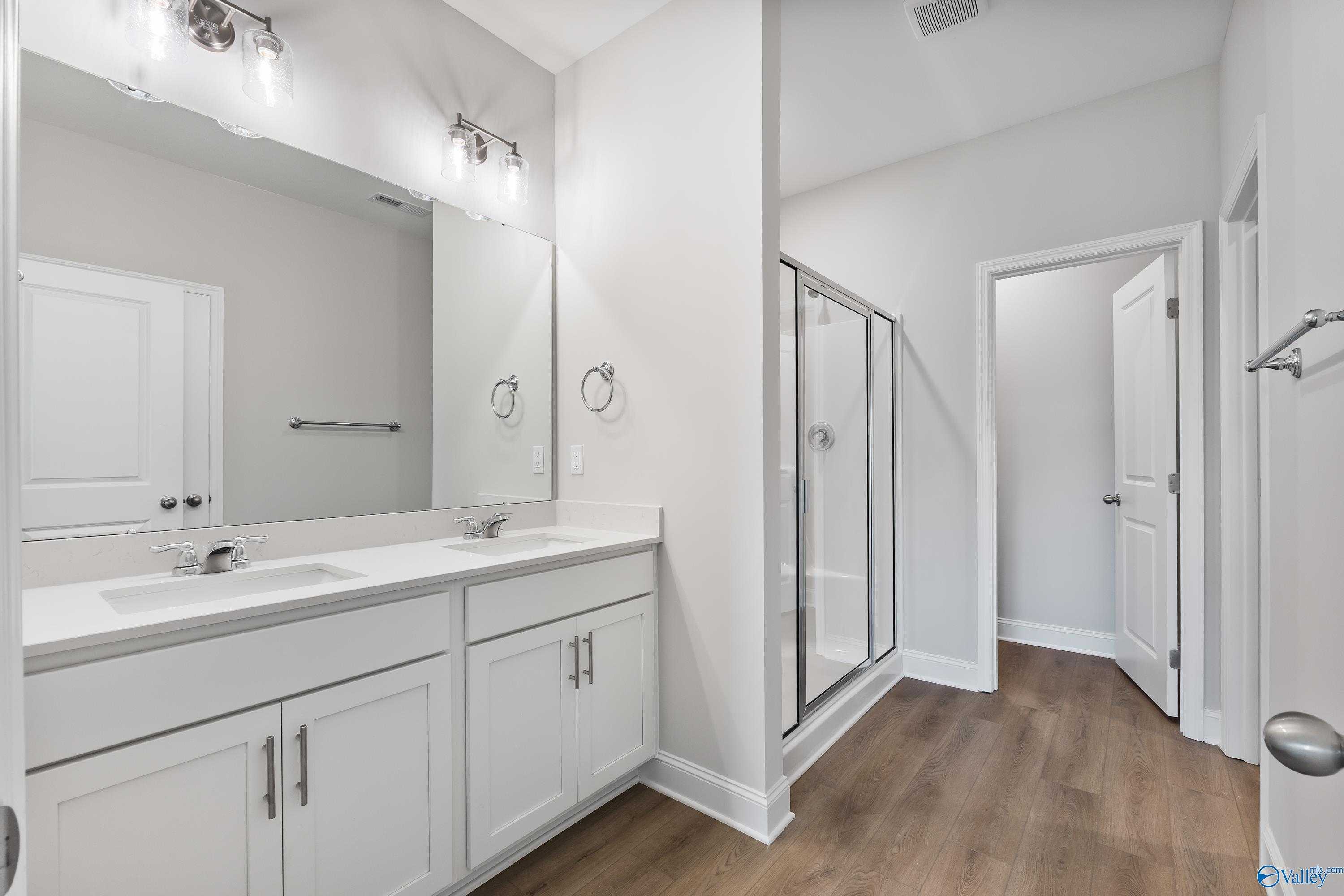 Modern master bathroom with double vanity, frameless glass shower, and luxury vinyl plank flooring in Davidson Homes The Daphne, Hazel Green, Alabama