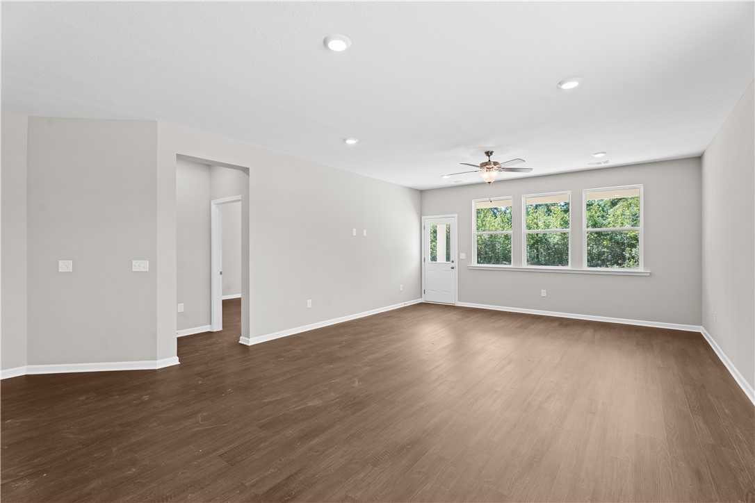 Bright living room with hardwood floors, ceiling fan, recessed lights, and large windows to lush trees in Evermore Homes The Orion, Cusseta, Alabama