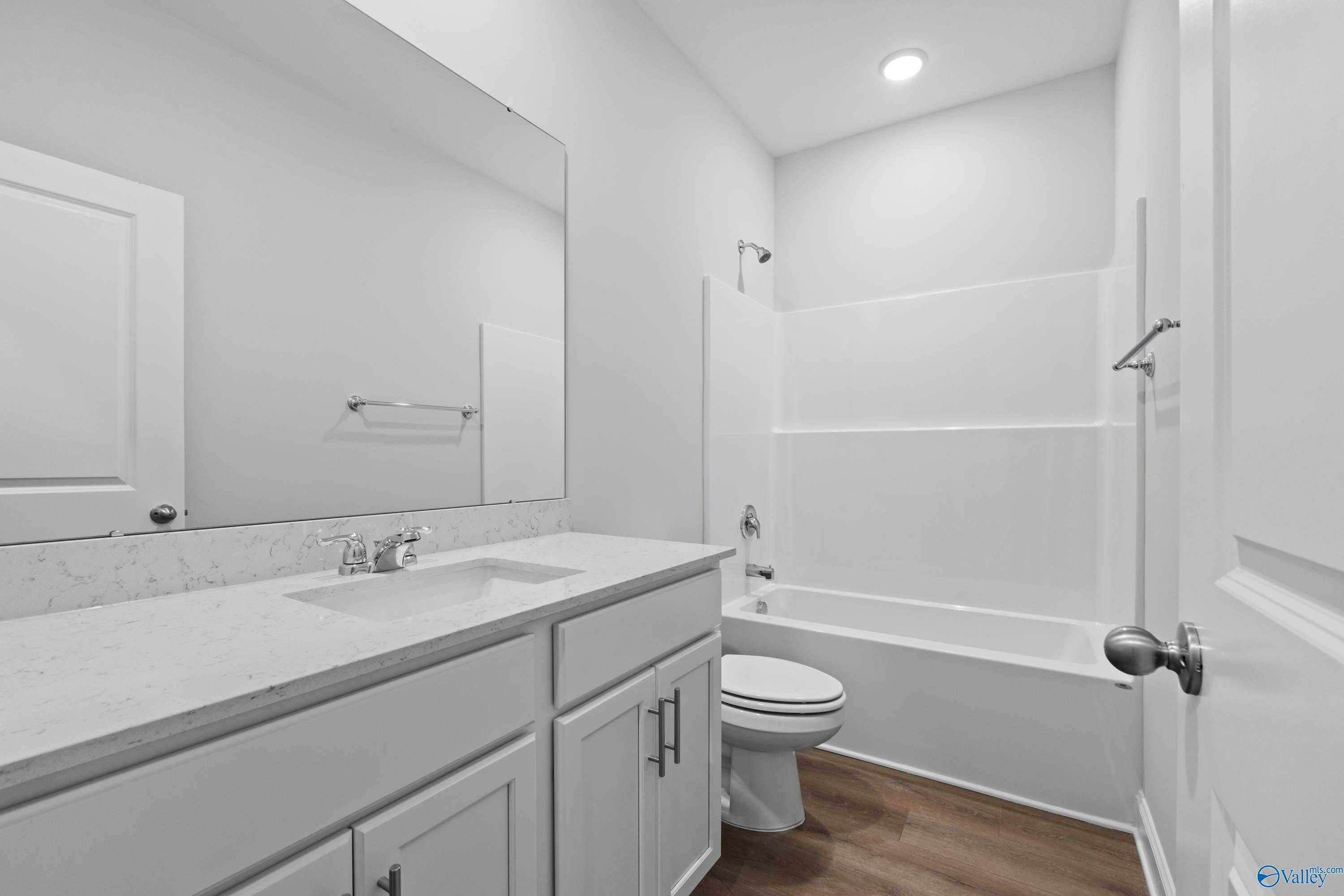 Bright bathroom with white quartz vanity, tub, walk-in shower and wood flooring in Davidson Homes The Asheville C, Huntsville AL