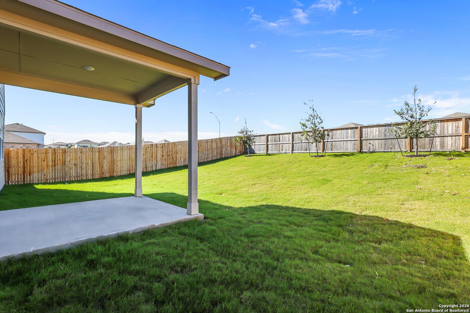 Covered back patio with concrete slab, lush green lawn, and wooden fence in Comanche Ridge, San Antonio, Texas Davidson Homes Douglas E