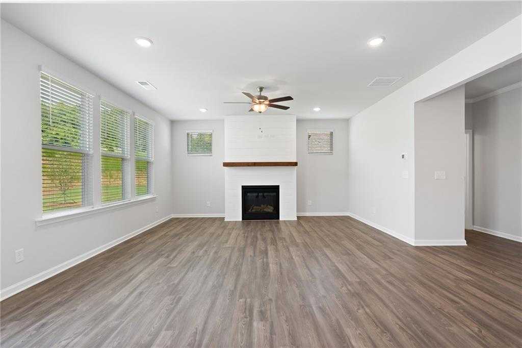 Spacious family room with white brick fireplace, hardwood floors, large windows, and ceiling fan in Davidson Homes The Hickory B, Winder, GA