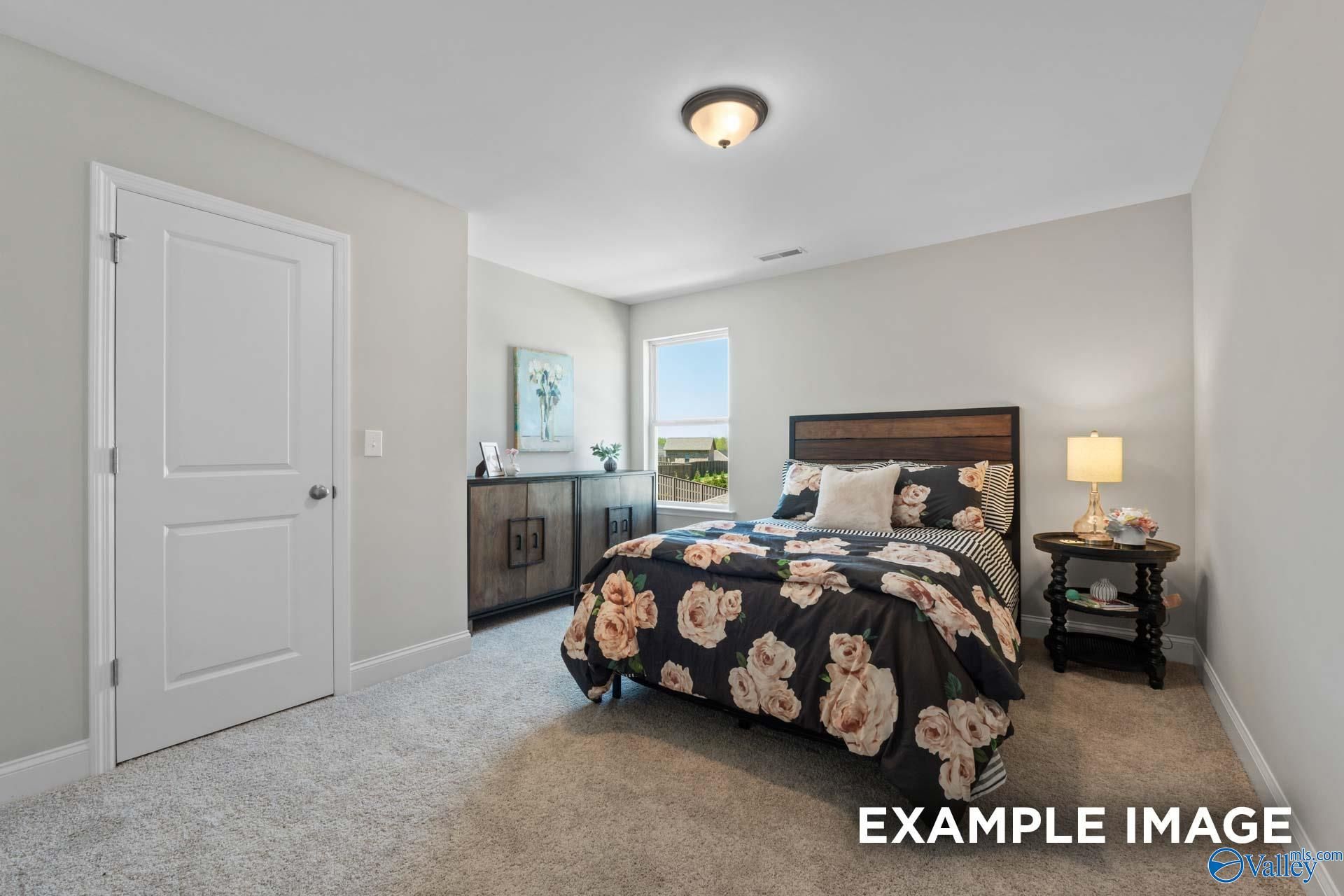 Cozy bedroom with floral black bedding on wooden headboard bed, nightstand lamp, and window view in Evermore Homes The Haven E, Owens Cross Roads, AL