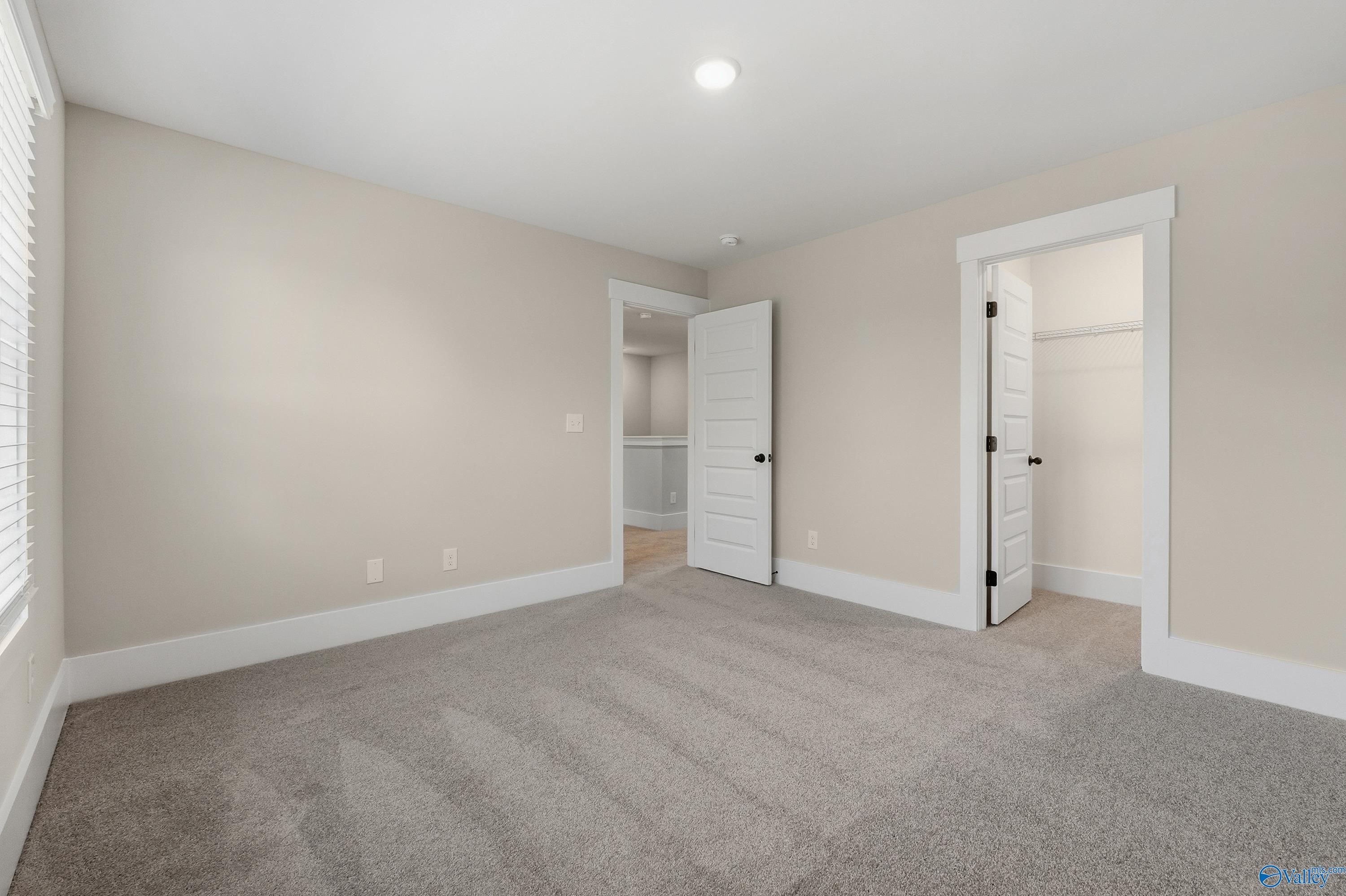Spacious bedroom with beige walls, gray carpet, open bathroom door, and closet in Davidson Homes The Shelby A, Athens, Alabama