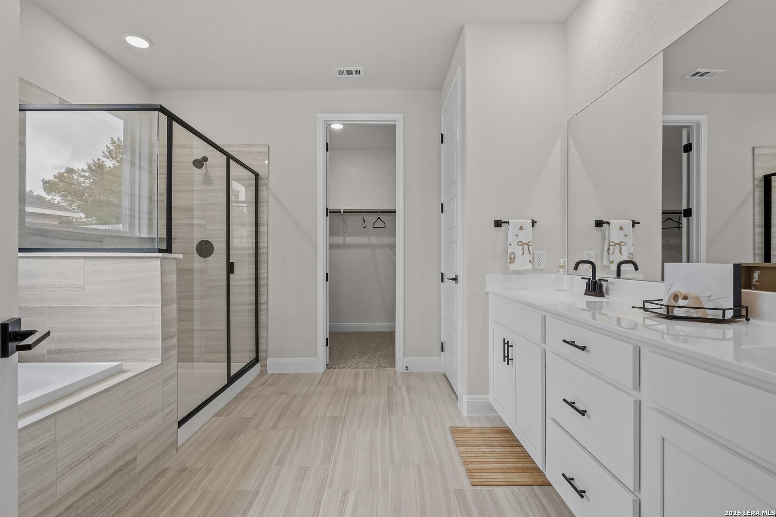 Modern master bathroom featuring frameless glass shower, soaking tub, double white vanity in The Lanier G, Castroville, Texas