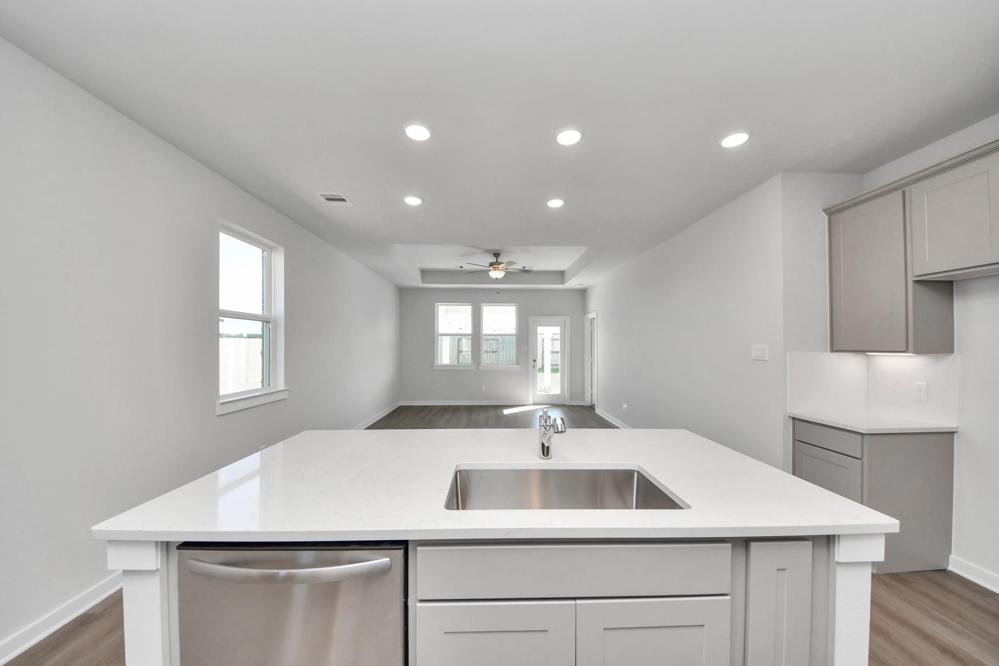 Open-concept kitchen island with sink and gray cabinetry in The Colorado G floor plan at Emberly, Beasley, Texas.