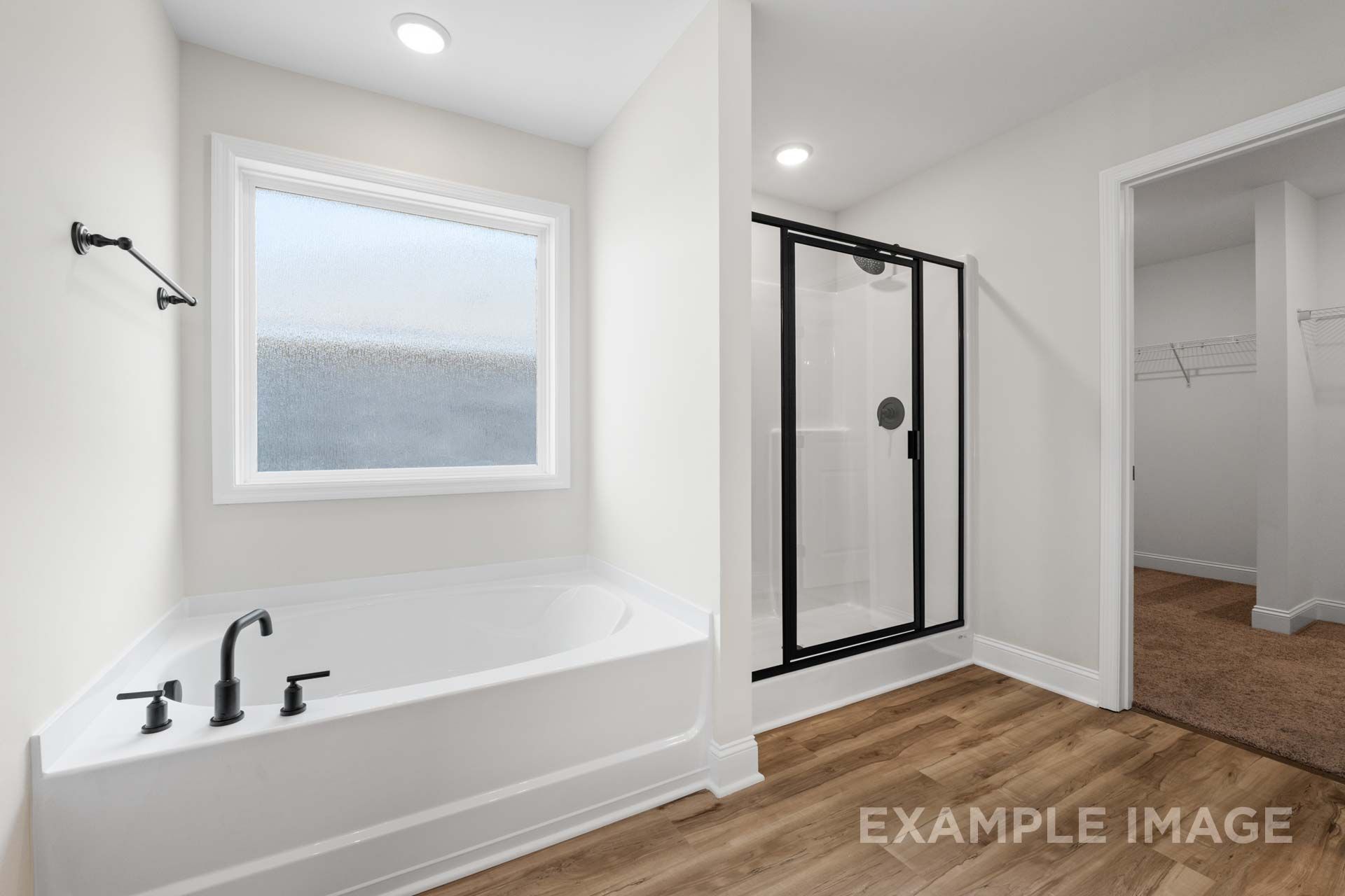 Spacious master bathroom in The Holly M featuring freestanding tub, glass shower, large frosted window, and walk-in closet