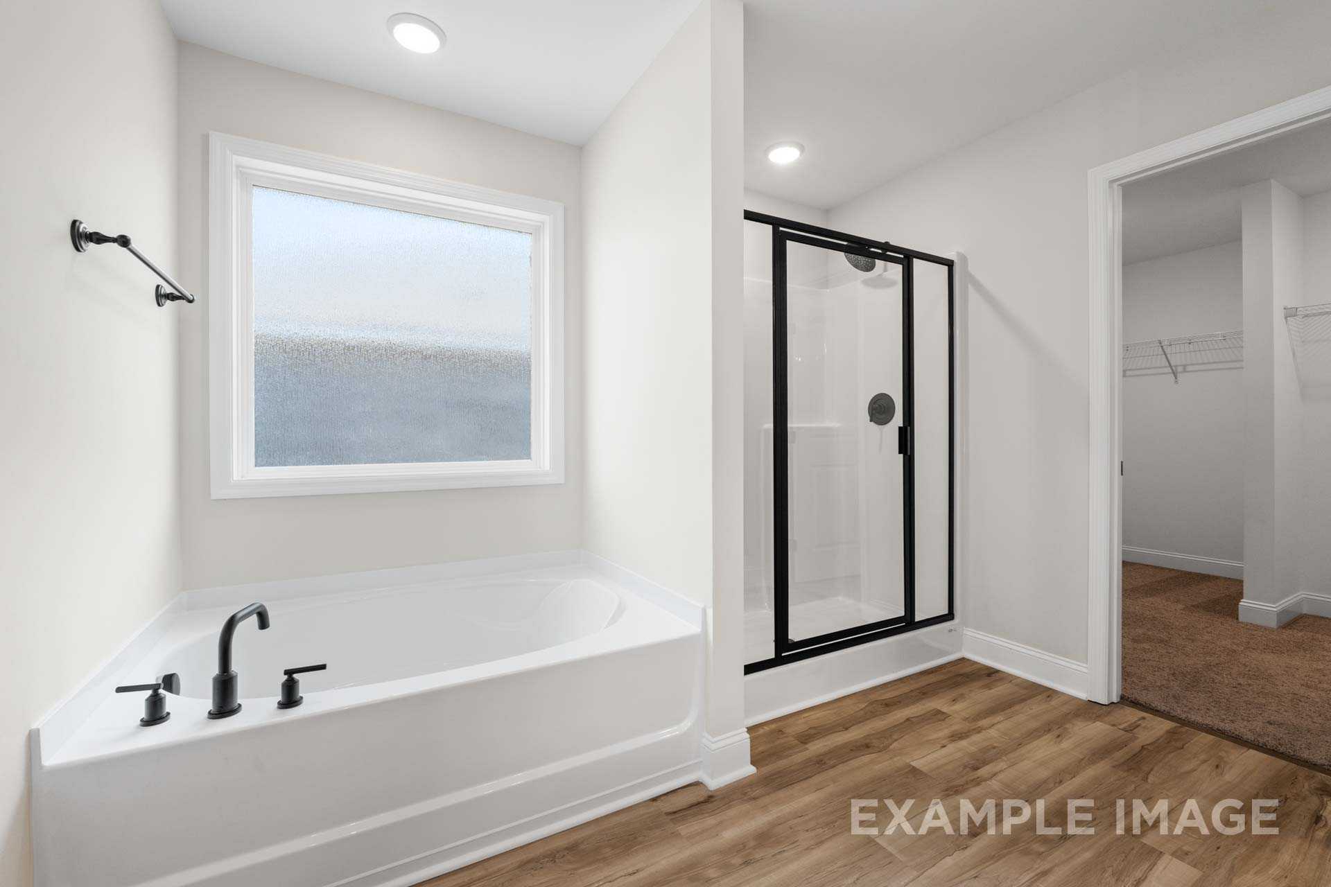 Spacious master bathroom in The Holly M featuring freestanding tub, glass shower, large frosted window, and walk-in closet