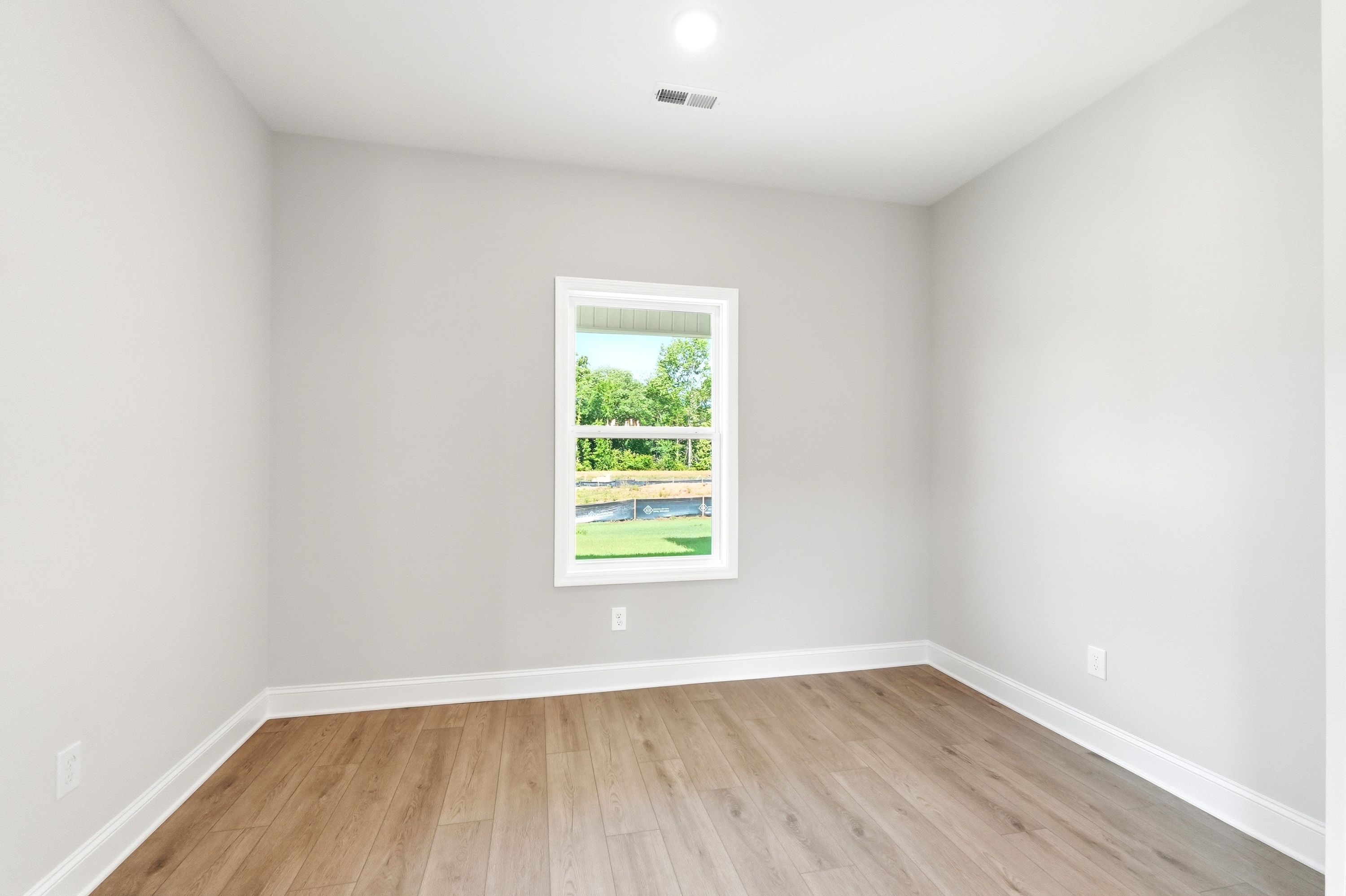 Bright, neutral bedroom with wood-look flooring and a single window in The Russell floor plan by Davidson Homes.