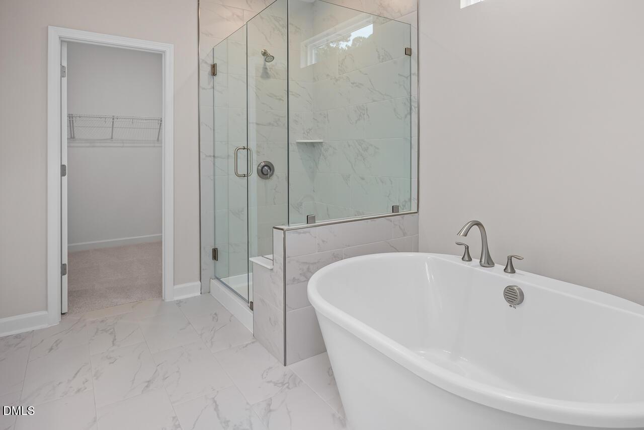 Modern primary bathroom with freestanding soaking tub and glass-enclosed marble shower in The Hickory II B, Zebulon, NC.