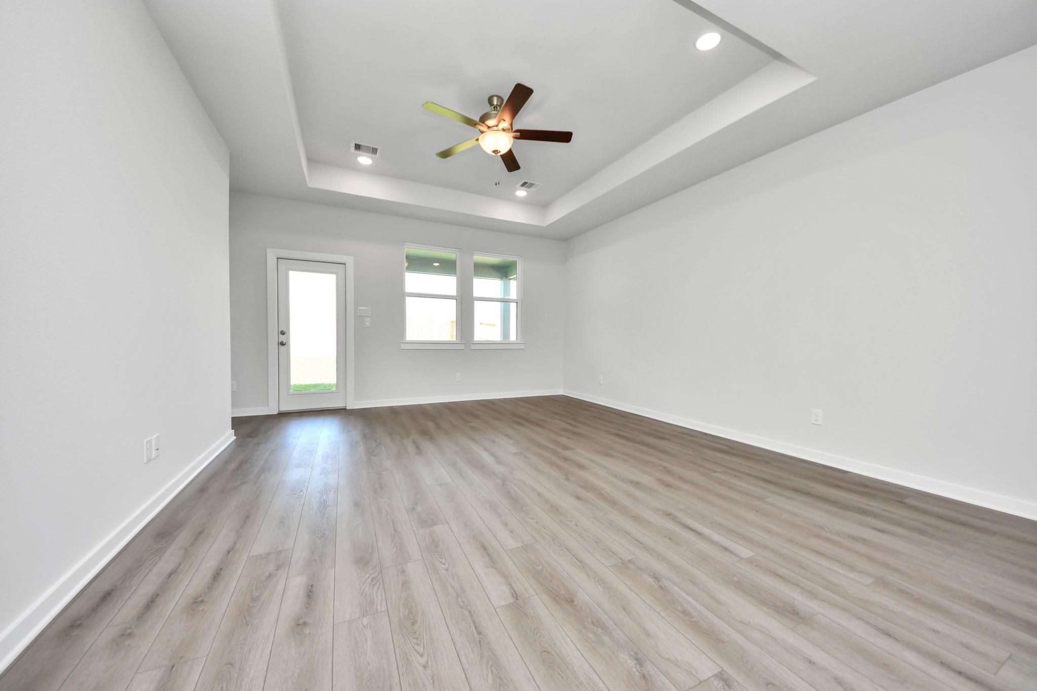 Spacious living area with tray ceiling and wood-style flooring in The Riviera A floor plan at Emberly in Beasley, Texas.