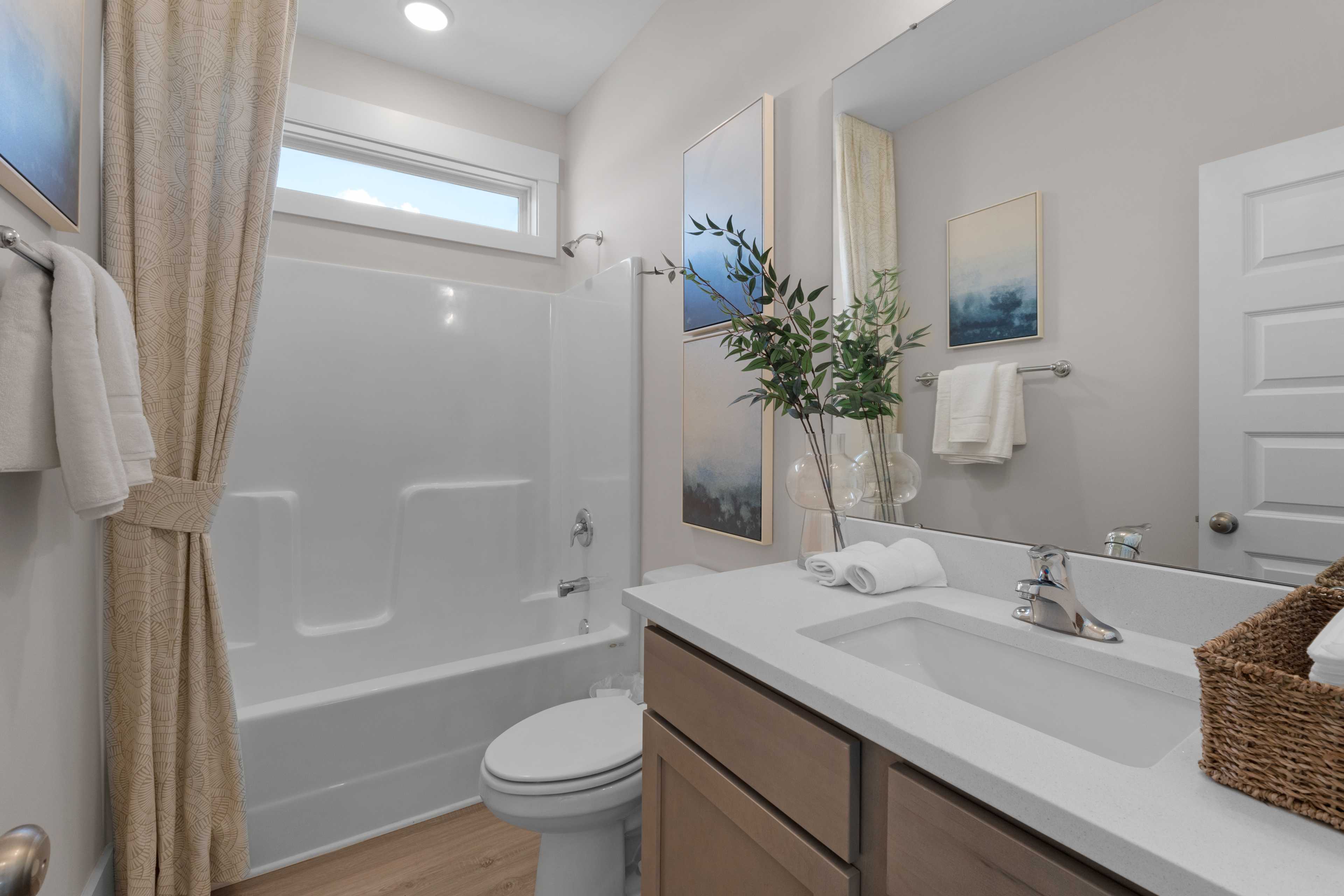 Bright bathroom in Hollon Meadow Decatur AL with white soaking tub, beige shower curtain, wooden vanity, and abstract wall art