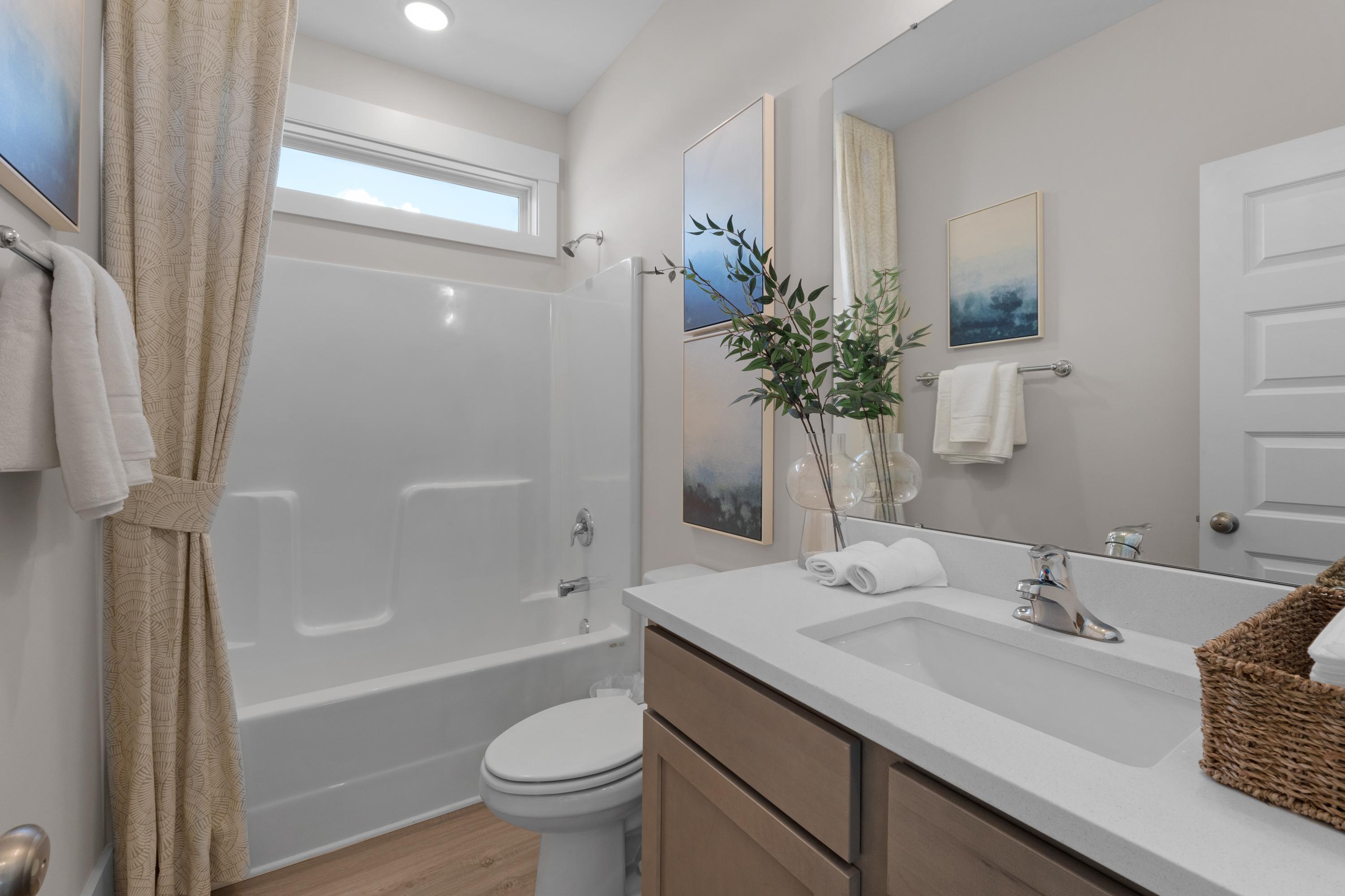 Bright bathroom in Hollon Meadow Decatur AL with white soaking tub, beige shower curtain, wooden vanity, and abstract wall art