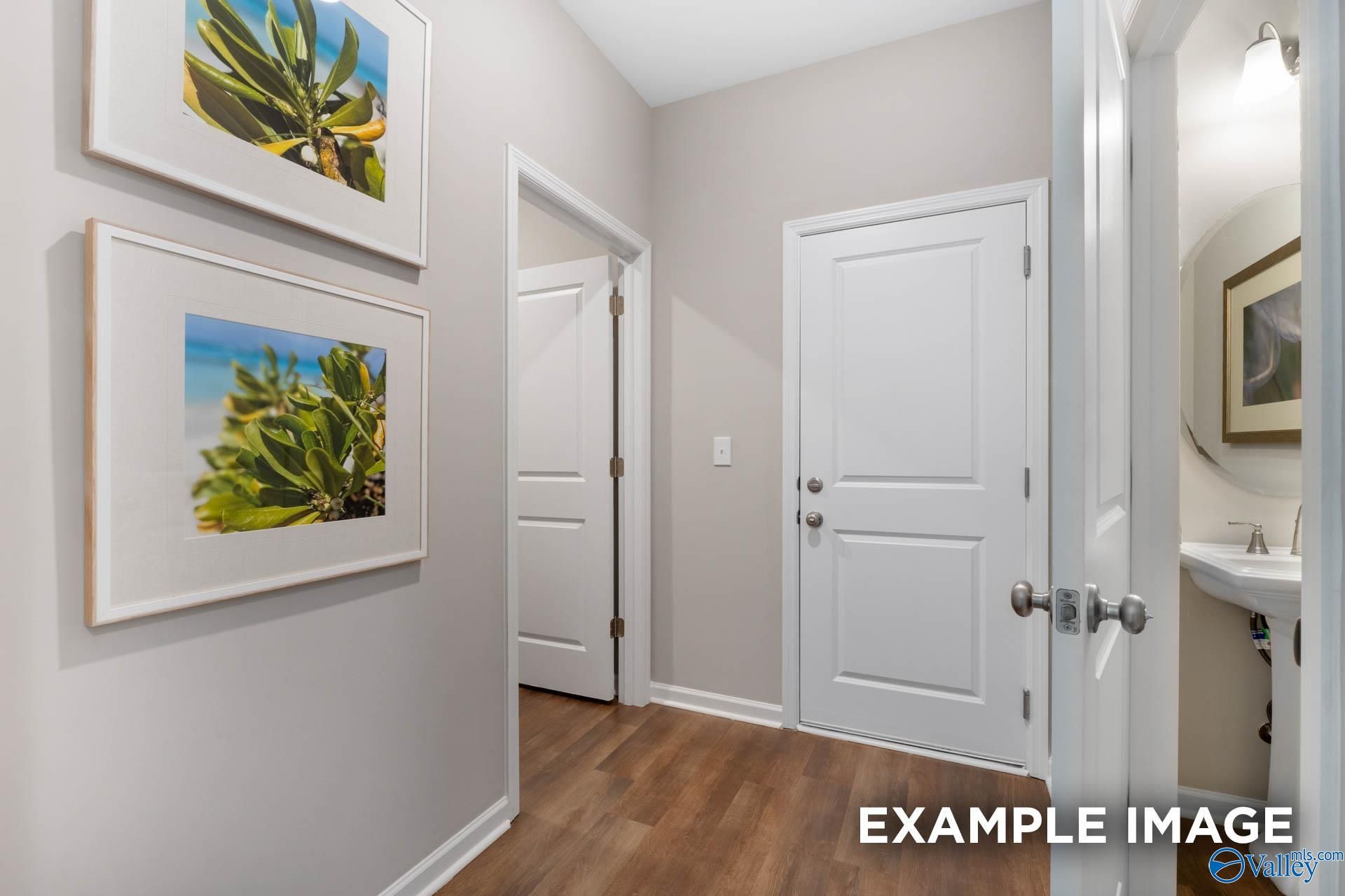 Elegant light gray hallway with hardwood floors, tropical artwork, and adjacent powder room in Davidson Homes The Stella, Madison Alabama