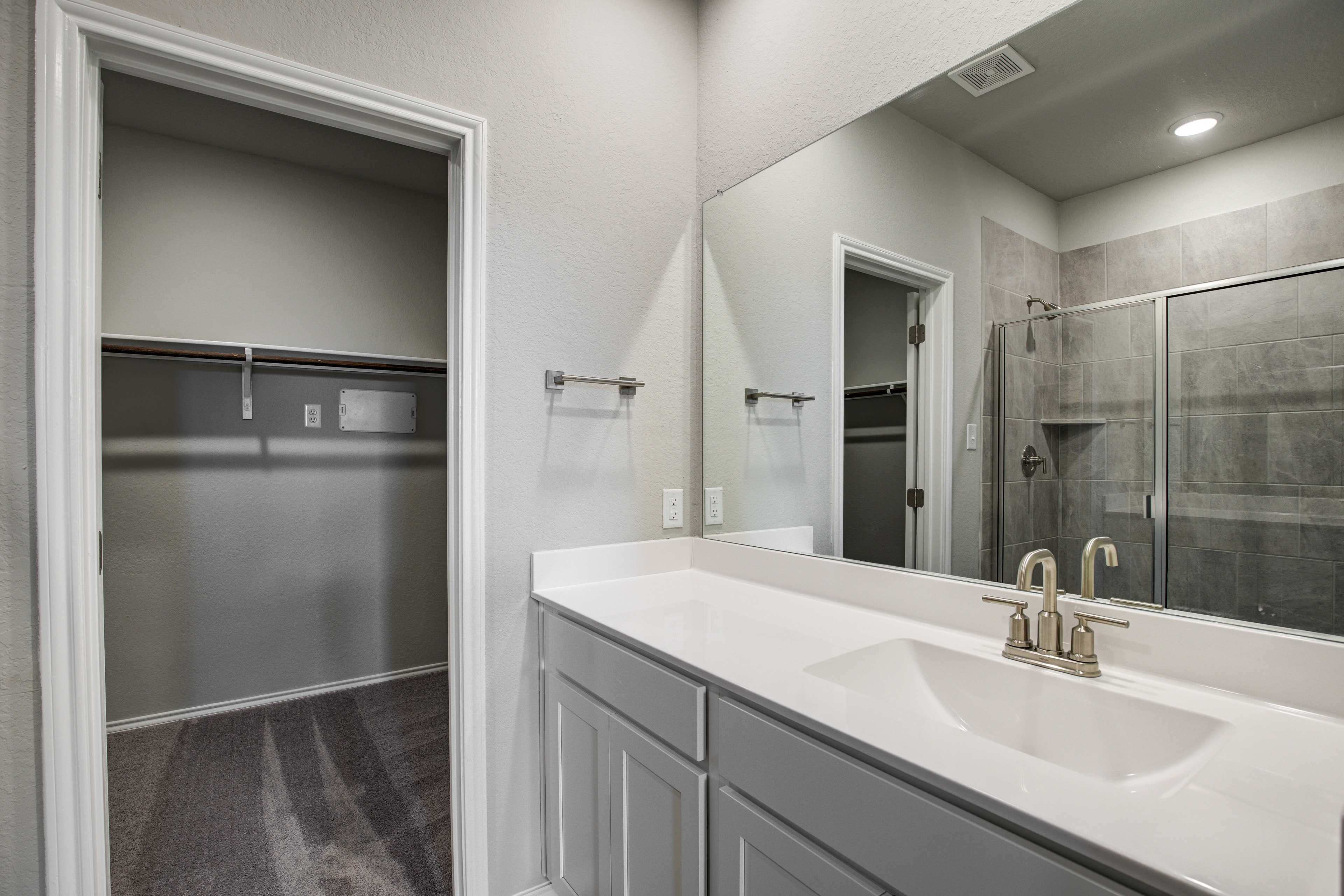Spacious master bathroom in The Blanco B with white vanity sink, large mirror, walk-in closet, and glass shower