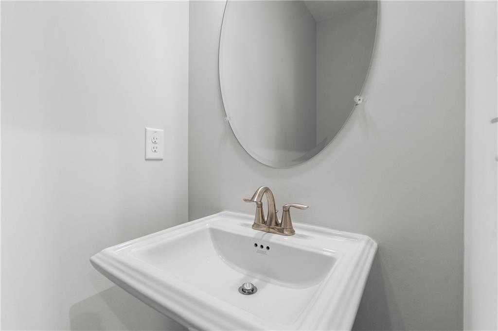 Elegant powder room with round mirror, white pedestal sink, and gold faucet in Davidson Homes The Monroe A, Emerson, Georgia