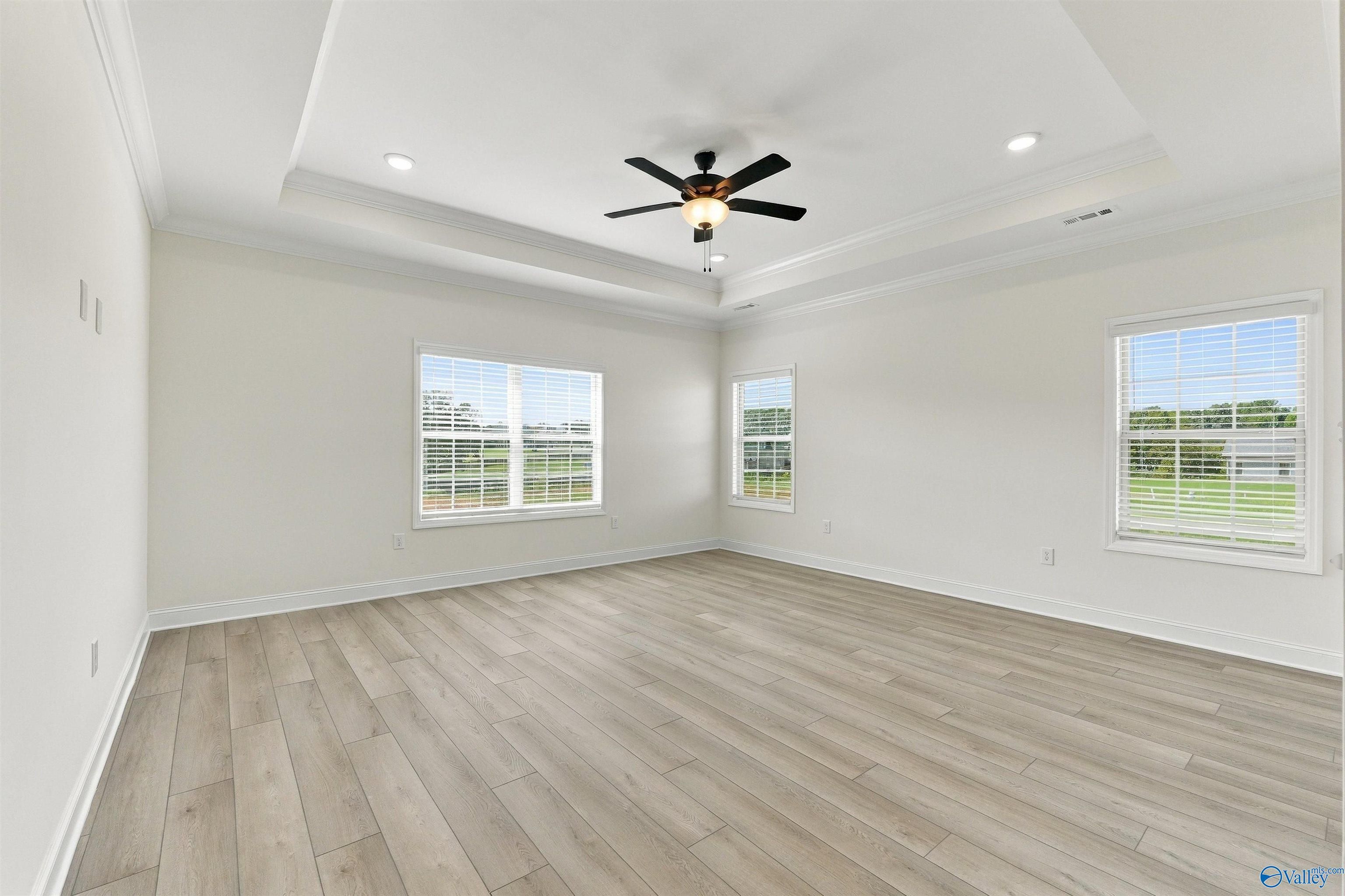 Bright primary bedroom with tray ceiling, ceiling fan, and vinyl plank flooring in Davidson Homes' The Valencia, Huntsville, AL