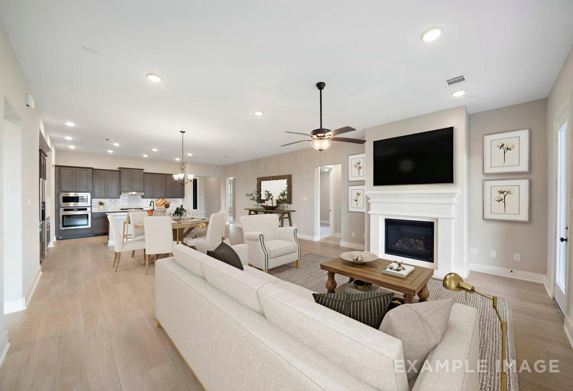 Spacious open-concept living room in The Elizabeth A home design with white sofas, gas fireplace, TV wall, and adjacent kitchen island