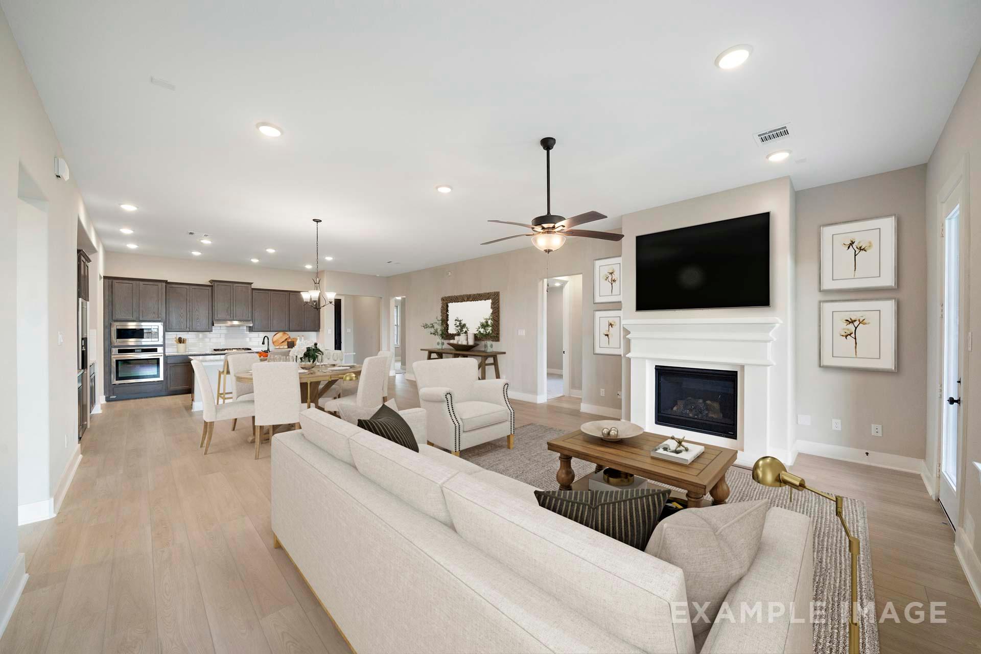 Spacious open-concept living room in The Elizabeth A home design with white sofas, gas fireplace, TV wall, and adjacent kitchen island