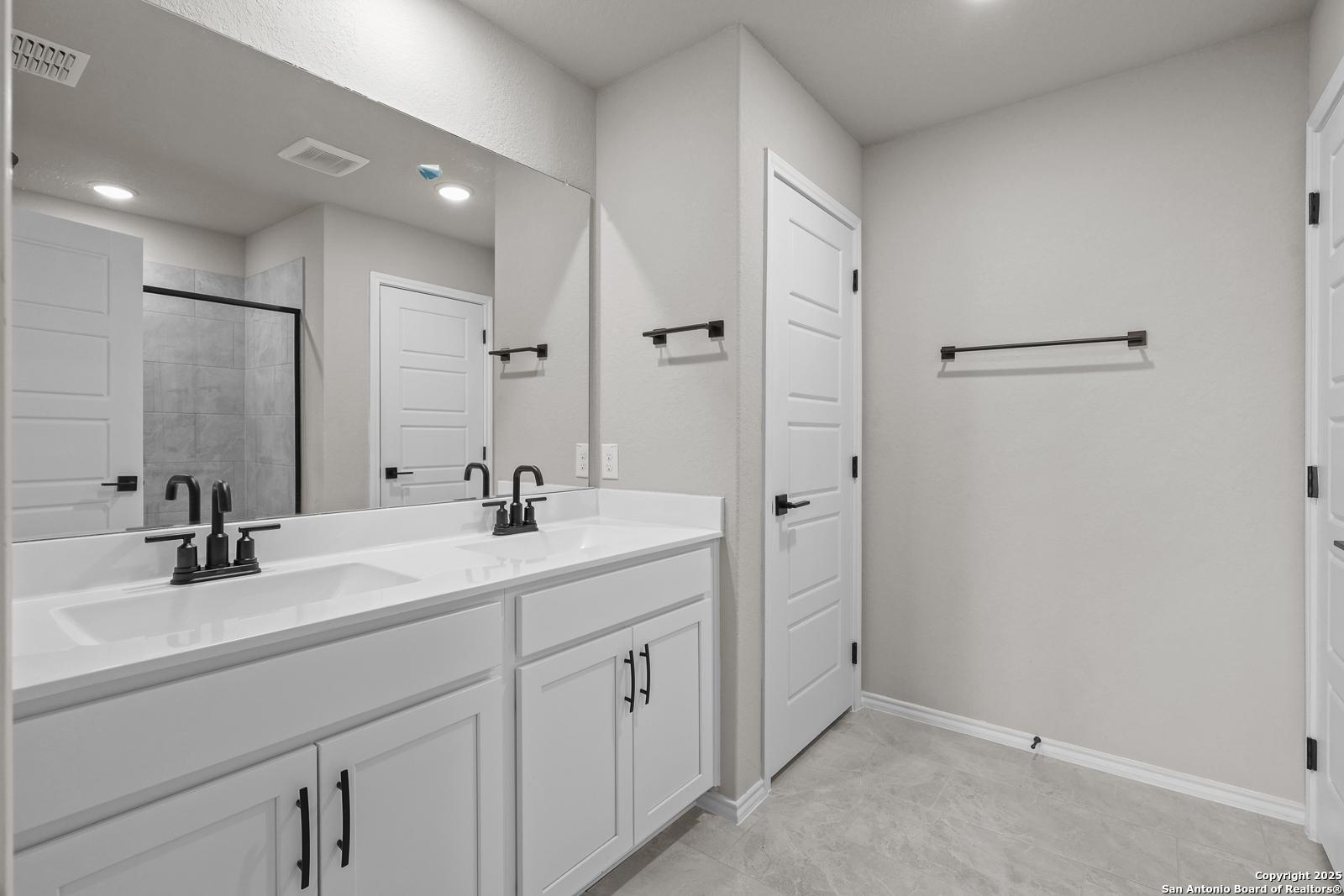 Elegant master bath with double white vanity, dual sinks, framed mirrors, and glass shower in Davidson Homes The Murray J, San Antonio