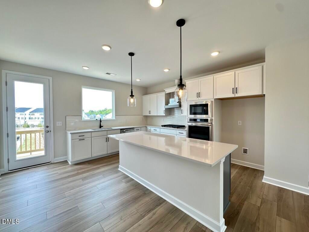 Modern white kitchen with quartz island, stainless steel appliances, pendant lights, and deck view in Davidson Homes The Avery, Knightdale, NC