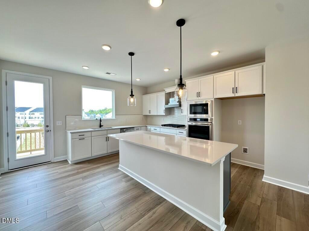 Modern white kitchen with quartz island, stainless steel appliances, pendant lights, and deck view in Davidson Homes The Avery, Knightdale, NC