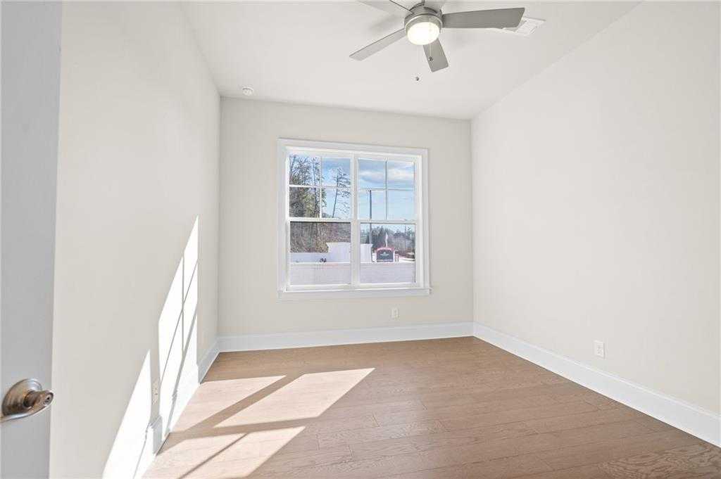 Bright empty bedroom with hardwood floors, ceiling fan, and large sunny window in Davidson Homes The Arlington A, East Cobb