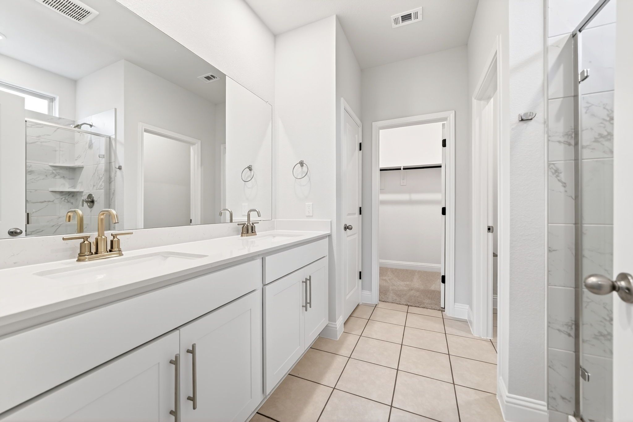 Modern master bathroom in The Redbud featuring a white dual-sink vanity, marble tile shower, and spacious walk-in closet.