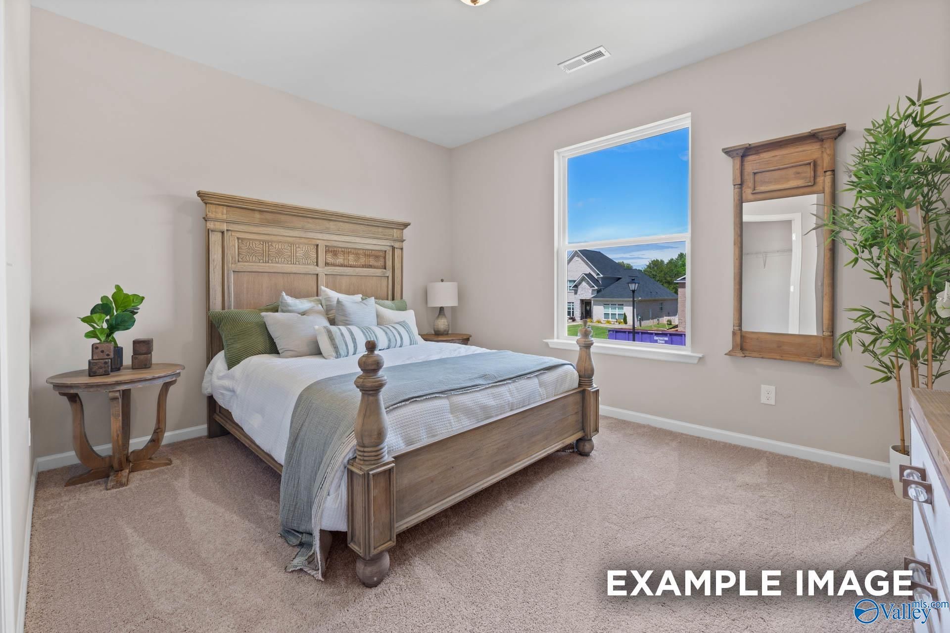 Inviting bedroom featuring carved wooden bed frame, neutral walls, large window with blue sky view in Evermore Homes The Arcadia M, Owens Cross Roads, AL