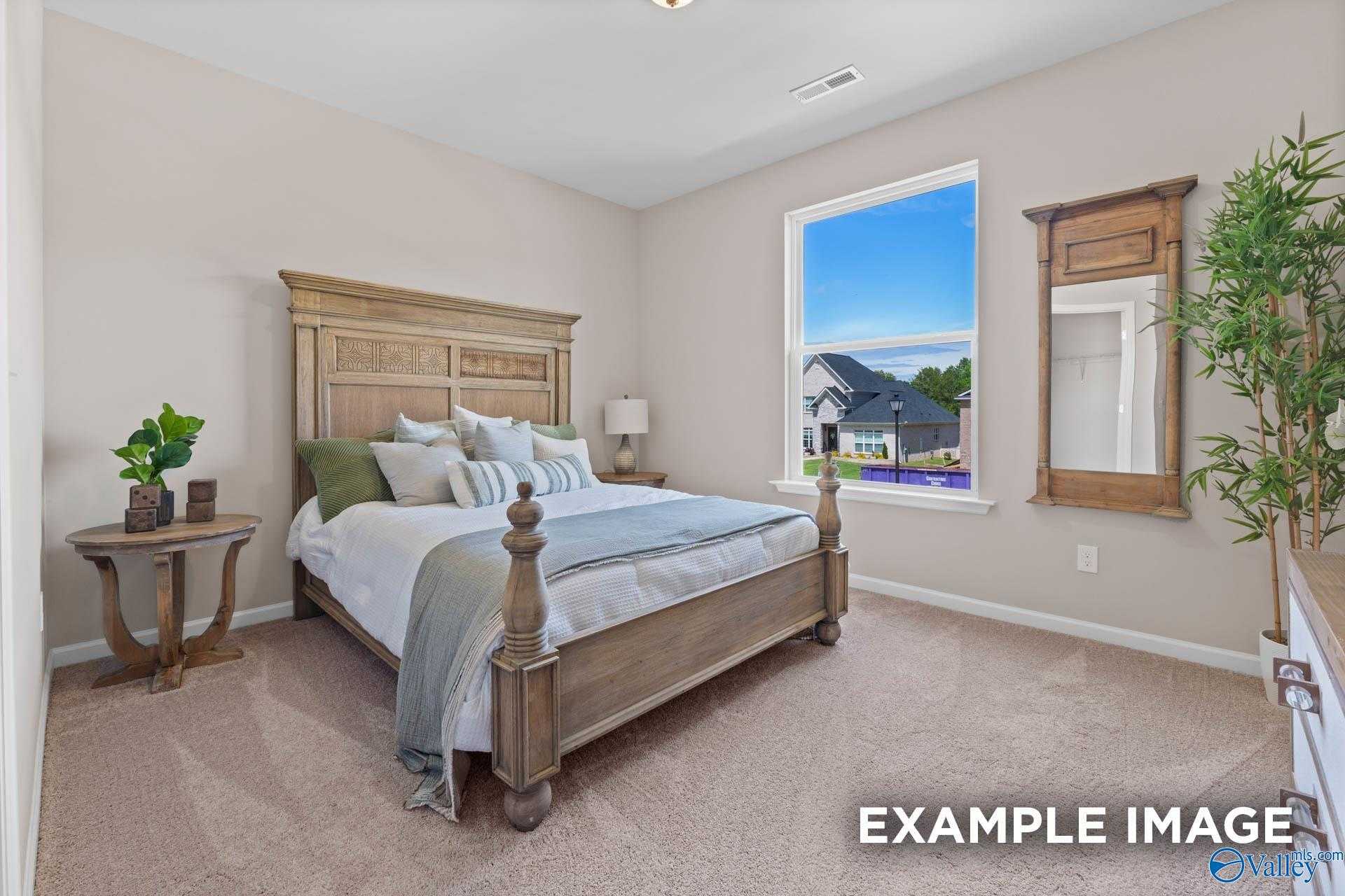 Inviting bedroom featuring carved wooden bed frame, neutral walls, large window with blue sky view in Evermore Homes The Arcadia M, Owens Cross Roads, AL