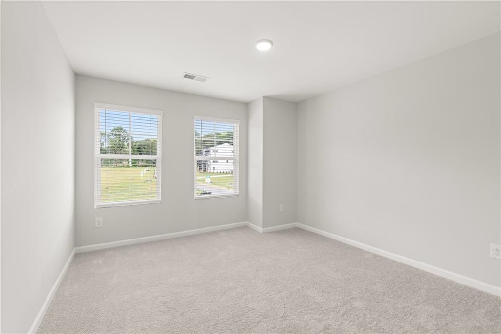 Bright, carpeted bedroom with neutral walls and windows in The Wake B floor plan by Davidson Homes in Cumming, Georgia.