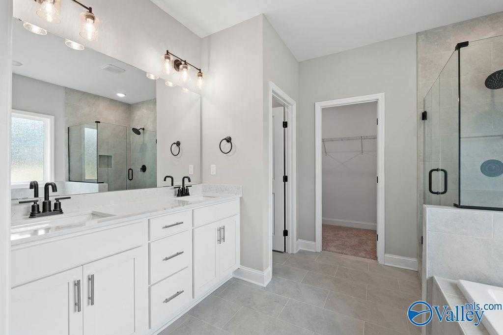 Modern master bathroom featuring double white vanity, frameless glass shower, and adjacent closet in Davidson Homes The Montgomery B, Hartselle, AL