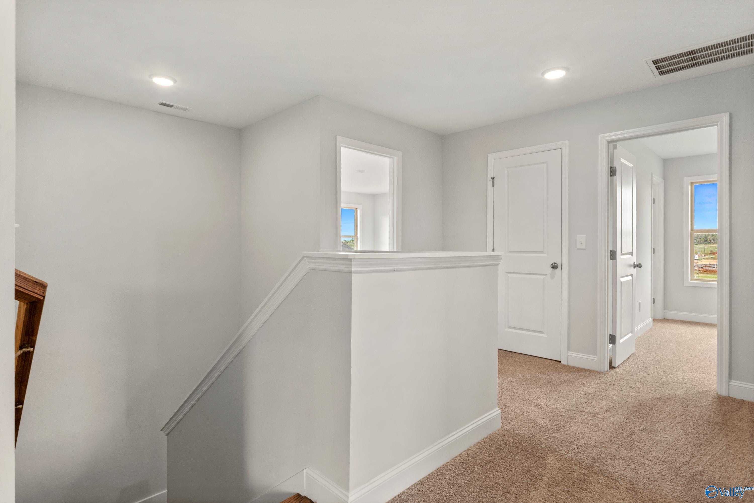 Bright upstairs hallway with white walls, open doors, and beige carpet in 4-bedroom The Chelsea C home, Creekside, Harvest, Alabama