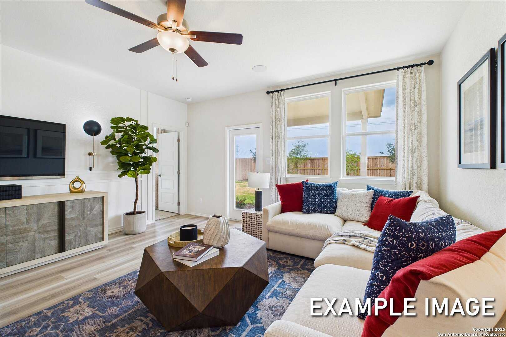 Cozy living room featuring plush white sectional sofa, mounted TV, and large windows overlooking backyard in Davidson Homes The Brazos C, San Antonio