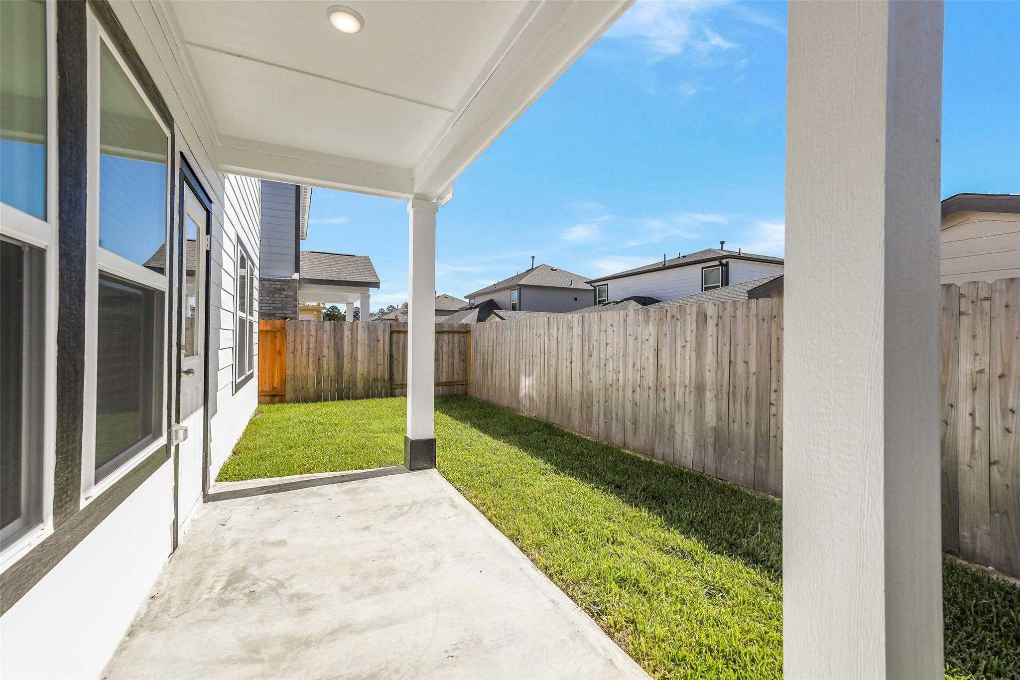 Covered back patio with lush green lawn, wooden privacy fence, and neighborhood view in Davidson Homes The Rio Grande H, Magnolia, Texas