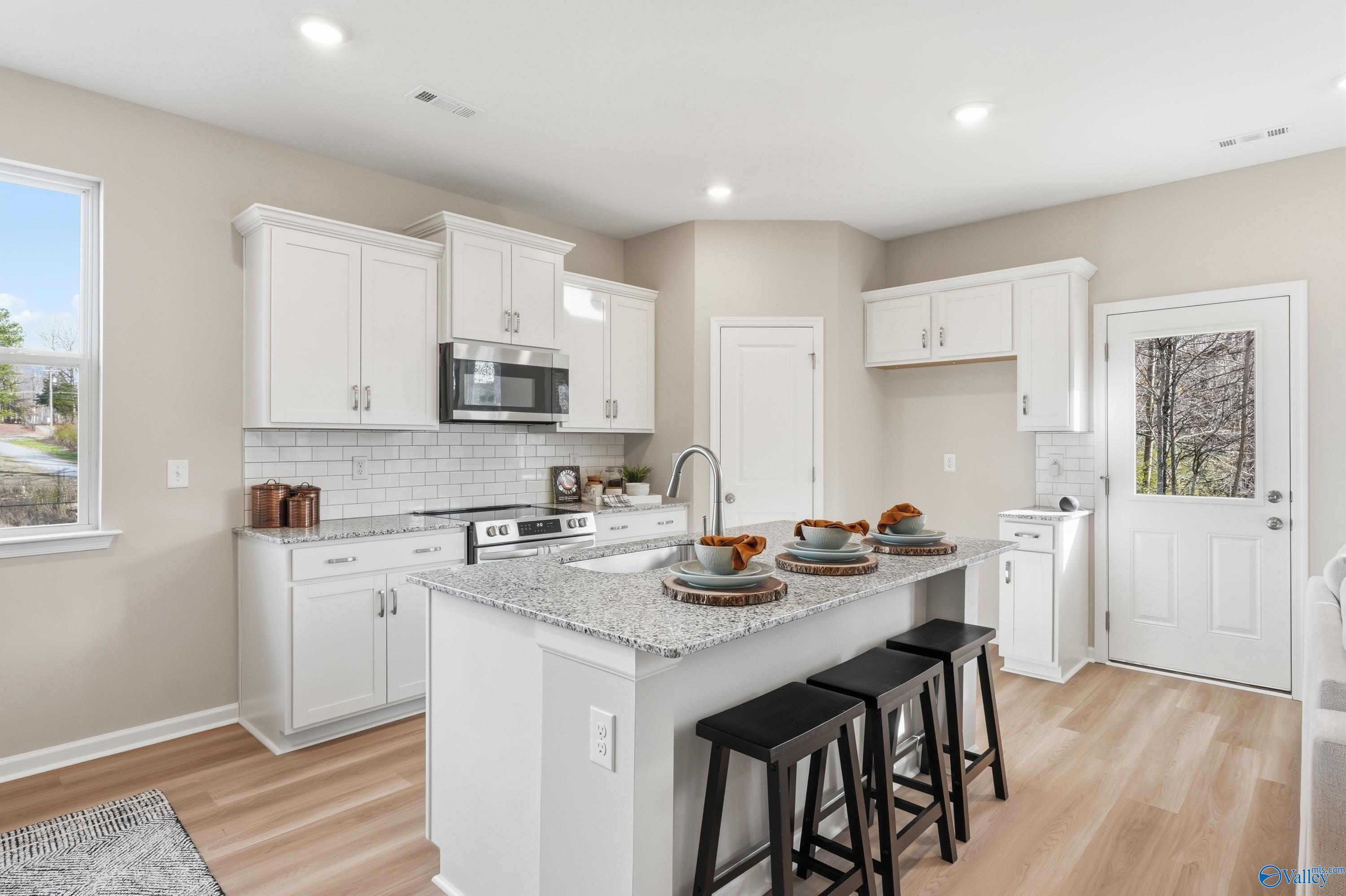 Modern white kitchen with granite island, bar stools, stainless appliances in The Polaris 3-bed home, Fayetteville, TN