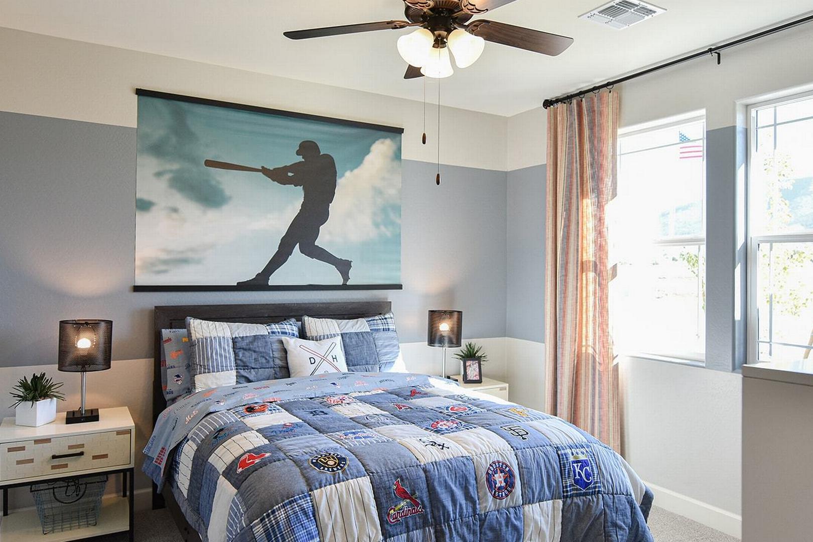 Boy's baseball-themed bedroom in The Summit E featuring batter wall mural, blue patchwork quilt, and ceiling fan