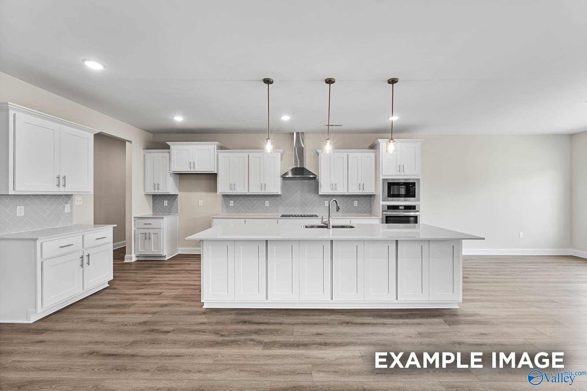 Modern white kitchen with large island, stainless appliances, pendant lights in Davidson Homes The Finleigh, Meridianville, AL