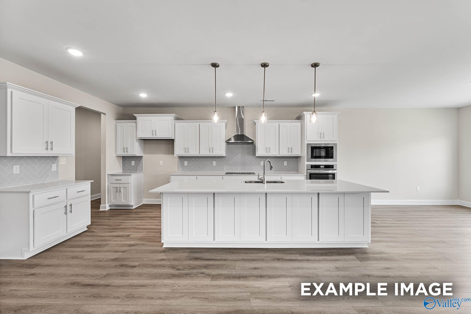 Spacious white kitchen with oversized island, stainless appliances, pendant lights in The Finleigh by Davidson Homes, Huntsville, AL