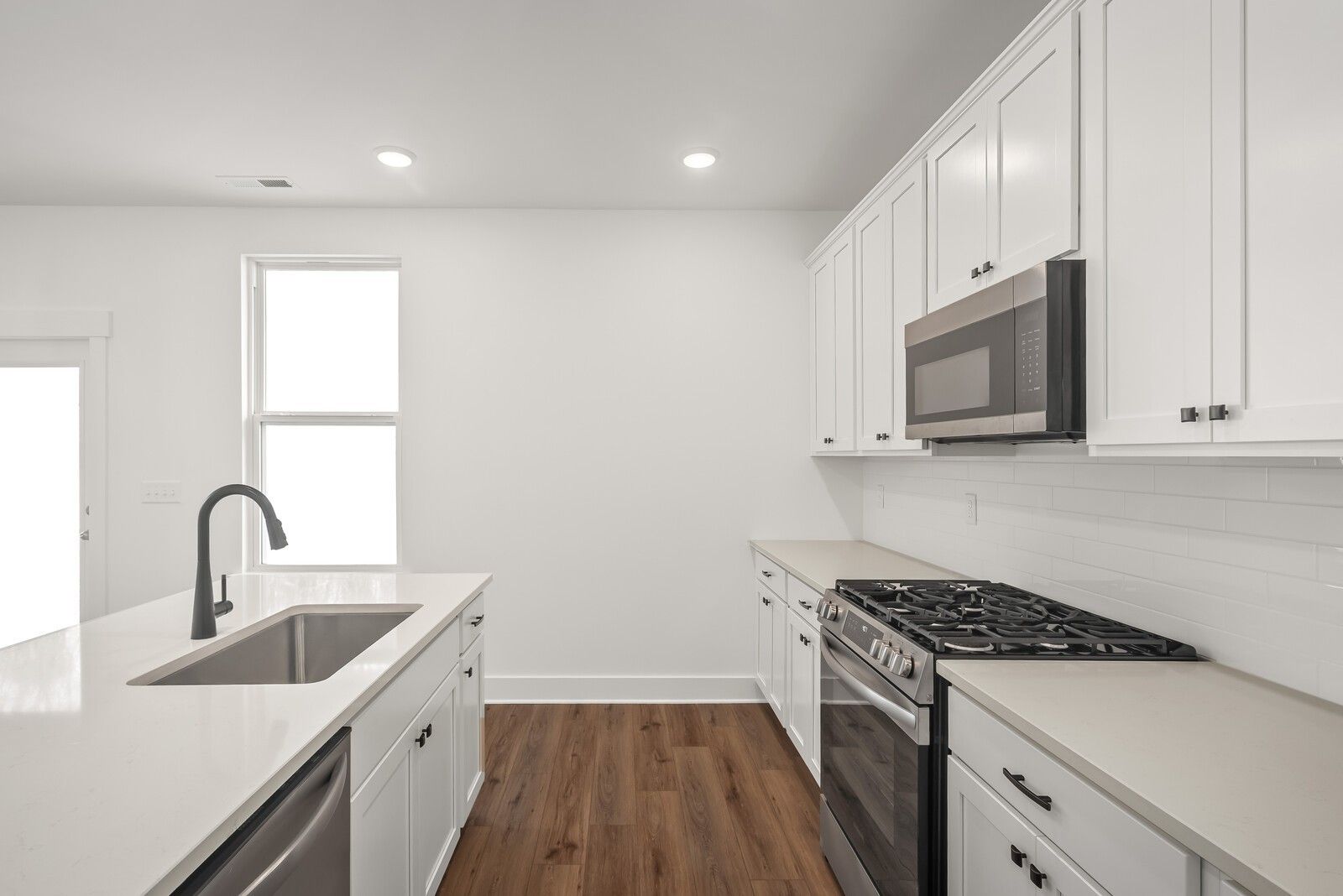 Modern white kitchen with large island, stainless appliances, quartz counters in Davidson Homes The Logan C, Gallatin, TN
