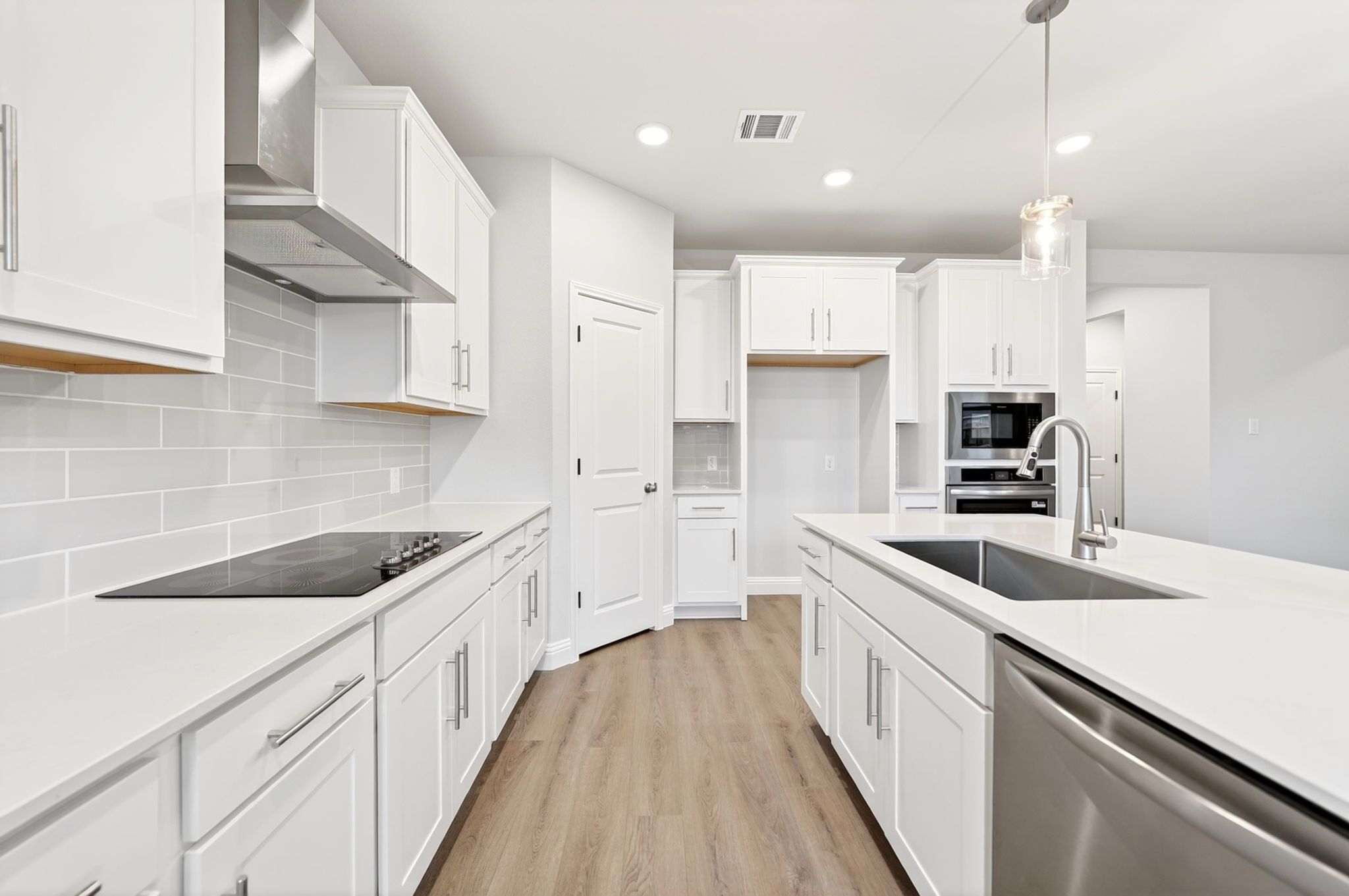 Modern kitchen in The Redbud featuring crisp white cabinets, quartz countertops, a large center island, and stainless steel.