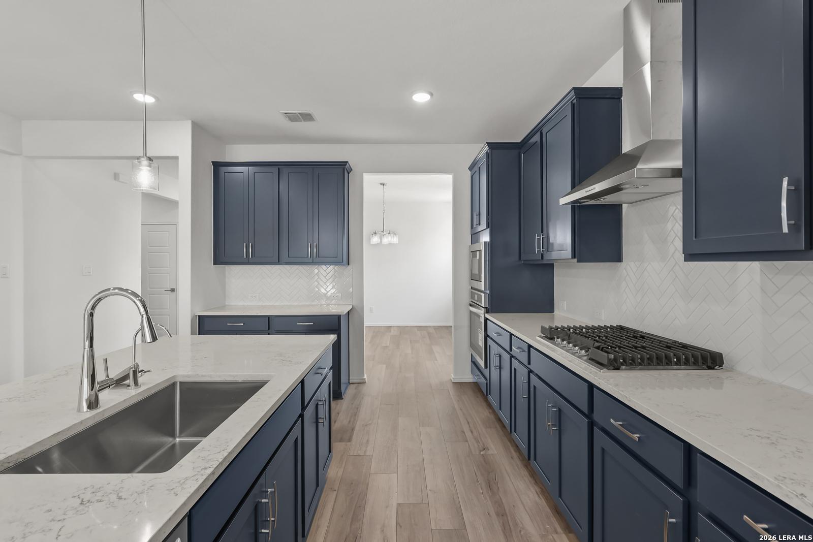 Modern navy blue kitchen with quartz island, stainless appliances, herringbone backsplash in Davidson Homes The Glenwood E, Elmendorf, TX