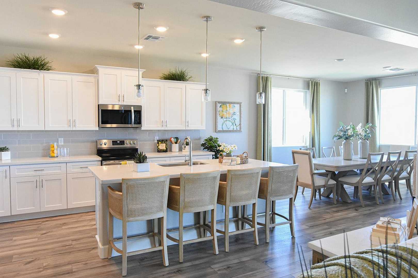 Spacious open-concept kitchen in The Summit B featuring white shaker cabinets, quartz island with bar stools, stainless appliances, and adjacent dining area
