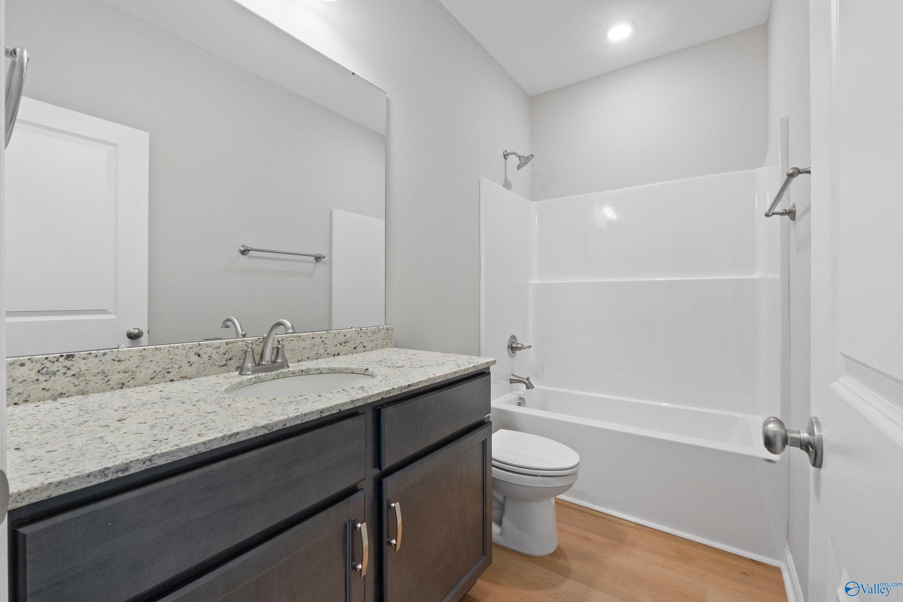Contemporary bathroom with granite vanity, deep tub, glass shower, and dark cabinets in Evermore Homes The Aurora, Harvest AL