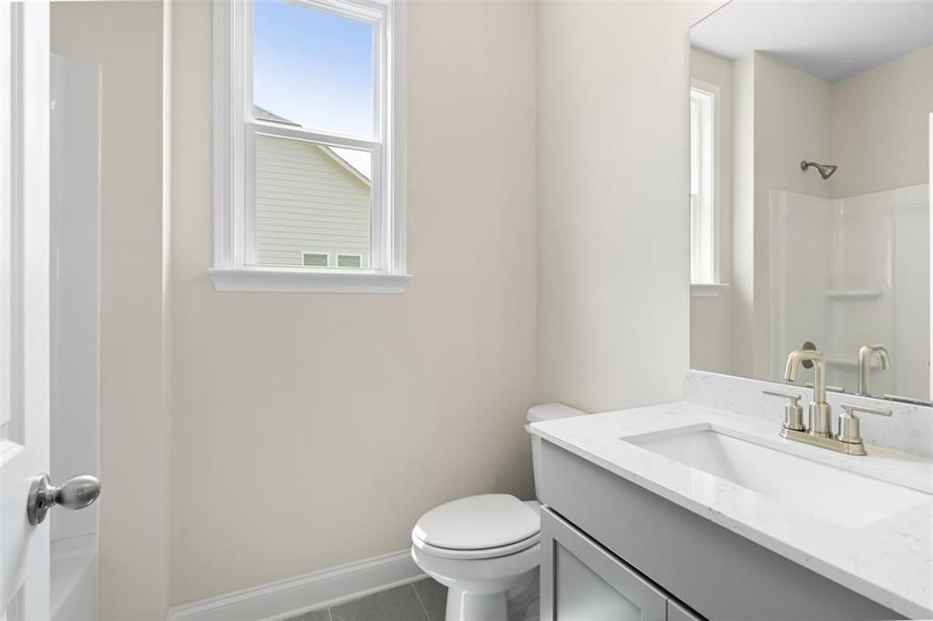 Modern bathroom with white quartz vanity, gold fixtures, tiled shower, and window view in Davidson Homes The Willow D at Wehunt Meadows, Hoschton